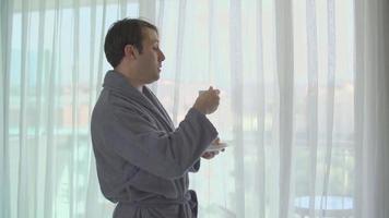 Drinking coffee in front of the window. Man drinking his coffee in front of the window with his bathrobe in the hotel. video