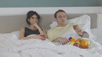Couple in bedroom. Watching TV. Couple lying in bed eating fruit watching TV. The man is happy and laughing.