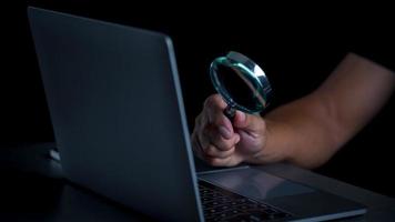A magnifying glass in a man's hand and he is looking at a notebook computer, the concept of searching for information in the internet world search technology Search Engine Optimization. photo
