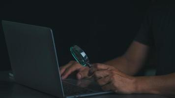 A magnifying glass in a man's hand and he is looking at a notebook computer. photo