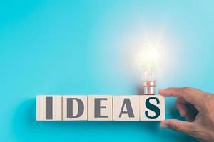 Hand holding a wooden block, a light bulb, all on a blue background, photo