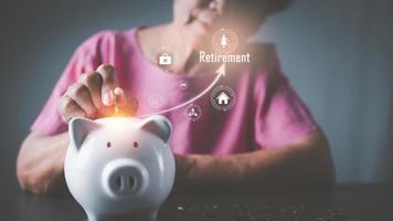 An old woman is putting money into a white piggy bank to save money for future use, photo