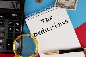 Tax deductions, the text is written in a white notepad, next to a calculator, a pen and a magnifying glass. photo