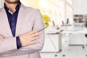 Businessman in gray business suit standing against the background of the office with crossed arms. copy space photo