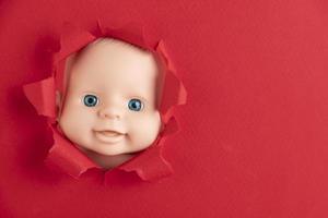 The doll's face peeks out from behind pieces of red paper, close-up. Copy space. photo