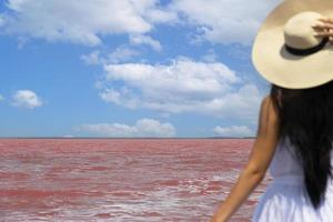 mujer viajera con sombrero mira el increíble lago de sal rosa exótico y el cielo azul. concepto de viaje de pasión por los viajes, espacio de copia para texto. enfoque selectivo. foto