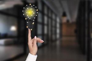 A woman's hand points to a glowing light bulb on the background of the office. Concept of innovation, ideas in business. photo