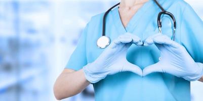Doctor woman, hands in medical blue gloves, making a heart shape. We love you. Copy space. photo