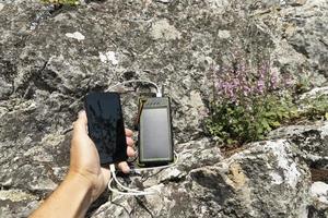 The smartphone is charged with a portable solar power bank charger on a rock during extreme travel. photo