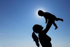 una niña sostiene a un niño en sus brazos contra el sol. fotografía de silueta. foto