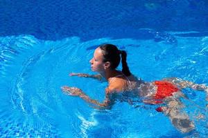 Top view of a tanned girl, female, model in a red swimsuit, swimming in the blue water of the pool. photo