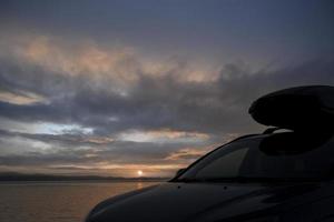 A car with a trunk with a cargo box, against the background of the sunrise over the sea. photo