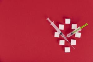 White sugar cubes and syringes on a red background in the form of the number zero. Copy the space. photo