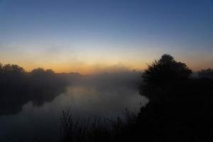 mañana nublada en un río europeo con hierba verde fresca bajo el sol. los rayos del sol a través del árbol. foto