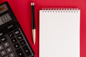 White notepad with calculator and stylish pen on a red background. Copy space. photo