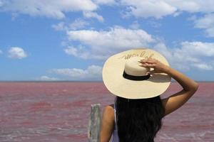 mujer viajera con sombrero mira el increíble lago de sal rosa exótico y el cielo azul. concepto de viaje de pasión por los viajes, espacio de copia para texto foto