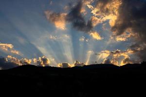 Sun light rays shining through dark clouds over mountains. photo