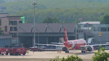 PHUKET, THAILAND NOVEMBER 29, 2019 - AirAsia plane parked at Phuket airport terminal. Fire trucks on the airfield. Aviation security concept