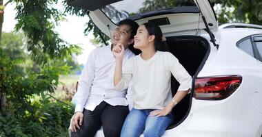 retrato de una feliz pareja asiática sentada y mirando la vista en la parte trasera de un auto. concepto de viaje y estilo de vida. video