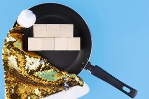 Concept for writing text on seven wooden cubes that lie in a frying pan and a Santa Claus hat. Copy space. photo