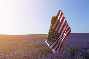 A young, dark-haired woman holding the flag of the United States of America against the sunny sky. Memorial Day and USA Independence Day concept. photo