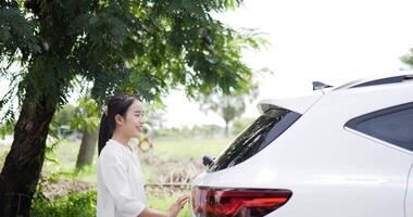 la donna asiatica chiude l'auto sul retro e guarda la fotocamera mentre si trova su una strada laterale. concetto di viaggio e stile di vita. video