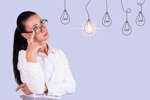 Portrait of a thoughtful young business woman with glasses looking at a light bulb as an Idea. Copy space. photo