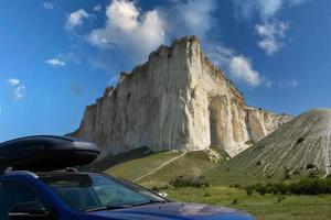 car for travel with a roof rack on a mountain road, against the backdrop of the White Rock. photo