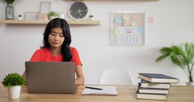 retrato de dos colegialas asiáticas que estudian en línea haciendo notas en un cuaderno con una computadora portátil en la mesa en casa. concepto de aprendizaje y educación a distancia. video