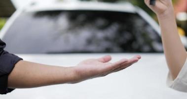 Close up of a woman handing over a car key to a mechanic man with blurred white car background. Car service concept. video