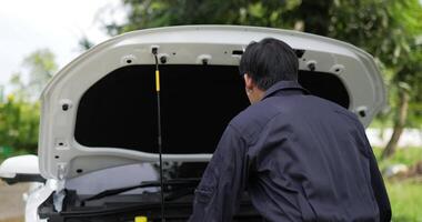 portret van een aziatische monteur die naar de motor van een pechauto kijkt en naar de camera kijkt die zijn duim omhoog laat zien. auto dienstverleningsconcept. video
