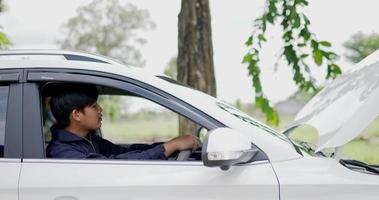 asiatischer automechaniker, der auf der fahrersitztür sitzt und den automotor betrachtet. Service-Wartungsversicherung mit Automotor. Auto-Service-Konzept. video