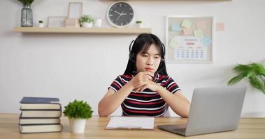 Ritratto di giovane asiatico servizio clienti agente di telemarketing che indossa l'auricolare guardando il laptop effettuare una videochiamata Internet per conferenze di lavoro. donna che prende nota.