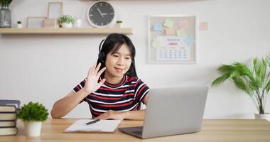 Portrait of Young Asian customer service support agent telemarketer wearing headset looking at laptop make business conference internet video call. Woman waving hand and making note.