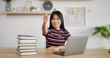 retrato de una colegiala asiática que estudia en línea a través de una laptop mostrando el pulgar hacia arriba en casa. concepto de aprendizaje y educación a distancia. video