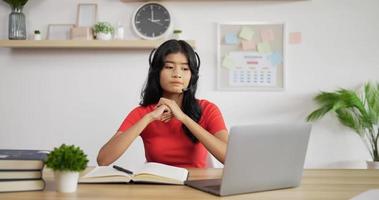 retrato de una colegiala asiática con auriculares estudiando en línea en una laptop en casa. concepto de aprendizaje y educación a distancia. video
