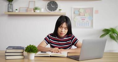 porträtt av asiatisk skolflicka studerar online läsa en lärobok med laptop på bordet hemma. distansundervisning och utbildning koncept. video