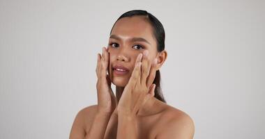 gelukkige aantrekkelijke jonge aziatische vrouw die mooi gezicht aanraakt na het aanbrengen van crème make-up. huidverzorging behandeling of cosmetische advertenties concept. video