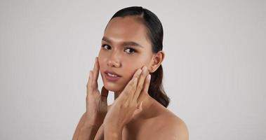heureuse jeune femme asiatique séduisante touchant un joli visage après avoir appliqué de la crème se maquiller. traitement de soins de la peau ou concept d'annonces cosmétiques.