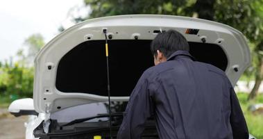 retrato de un mecánico asiático que mira el motor de un auto averiado y mira la cámara que muestra el signo de ok. concepto de servicio de coche. video