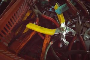 Old pliers in plastic basket. Second-hand tool for sale at tools market. Old pliers in tool tray. Toolkit of handyman. Mechanic hand tools. Used tools in second-hand market, Thailand. Many of pliers. photo