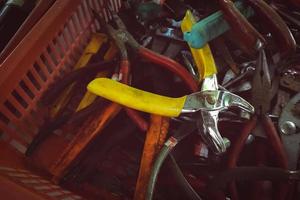 Old pliers in plastic basket. Second-hand tool for sale at tools market. Old pliers in tool tray. Toolkit of handyman. Mechanic hand tools. Used tools in second-hand market, Thailand. Many of pliers. photo