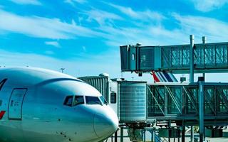 aerolínea comercial estacionada en el puente de reacción para el despegue de pasajeros en el aeropuerto. puente de embarque de pasajeros de aviones acoplado con cielo azul y nubes blancas. vuelo de salida de la aerolínea internacional. foto