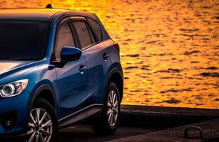 Blue compact SUV car with sport and modern design parked on concrete road by sea at sunset. Environmentally friendly technology. Hybrid and electric car technology. Car parking space. summer travel. photo