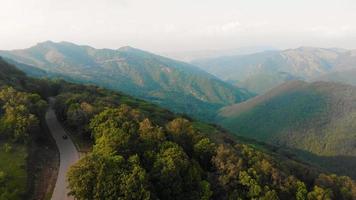 Flygfoto vit bil färdas i vacker bergig terräng. en bil som kör på en asfaltväg med vackert landskap i Georgien video