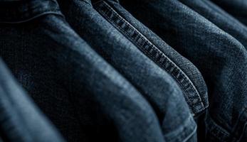 Selective focus on jacket jeans hanging on rack in clothes shop. Denim jeans with jeans pattern. Textile industry. Jeans fashion and shopping concept. Clothing concept. Denim jacket on rack for sale. photo