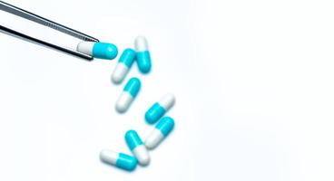 Forceps pick white-blue capsule from group of capsule pills. Drugs choose. Antibiotic drug selection. Antibiotic drug resistance concept. QA and QC in pharmaceutical factory concept. Drugs of choice. photo