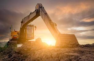 Backhoe parked at construction site after digging soil. Bulldozer on sunset sky and clouds background. Digger after work. Earth moving machine at construction site at dusk. Digger with dirt bucket. photo