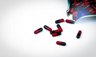 Top view of red and black capsule pills on stainless steel drug tray and some capsule pills on white background. Pharmacy drugstore product. Capsule pills count. Pharmaceutical industry. Healthcare. photo