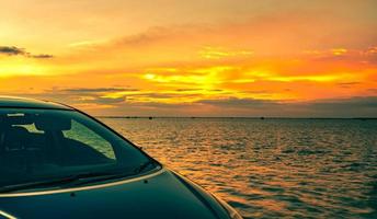 Blue compact SUV car with sport and modern design parked on concrete road by the sea at sunset. Electric car technology and business. Hybrid auto and automotive. Road trip travel on summer vacation. photo